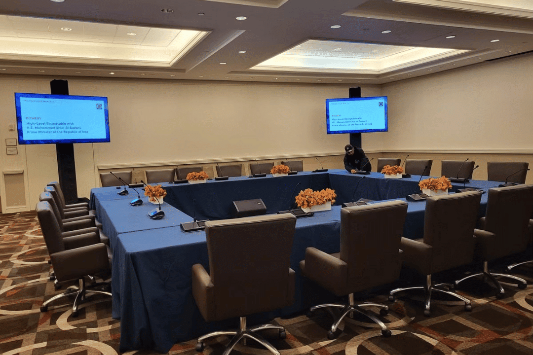 Corporate meeting room setup with conference table, microphones, and presentation screens for multilingual business discussion