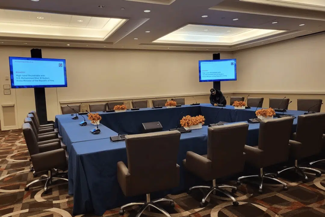 Corporate meeting room setup with conference table, microphones, and presentation screens for multilingual business discussion