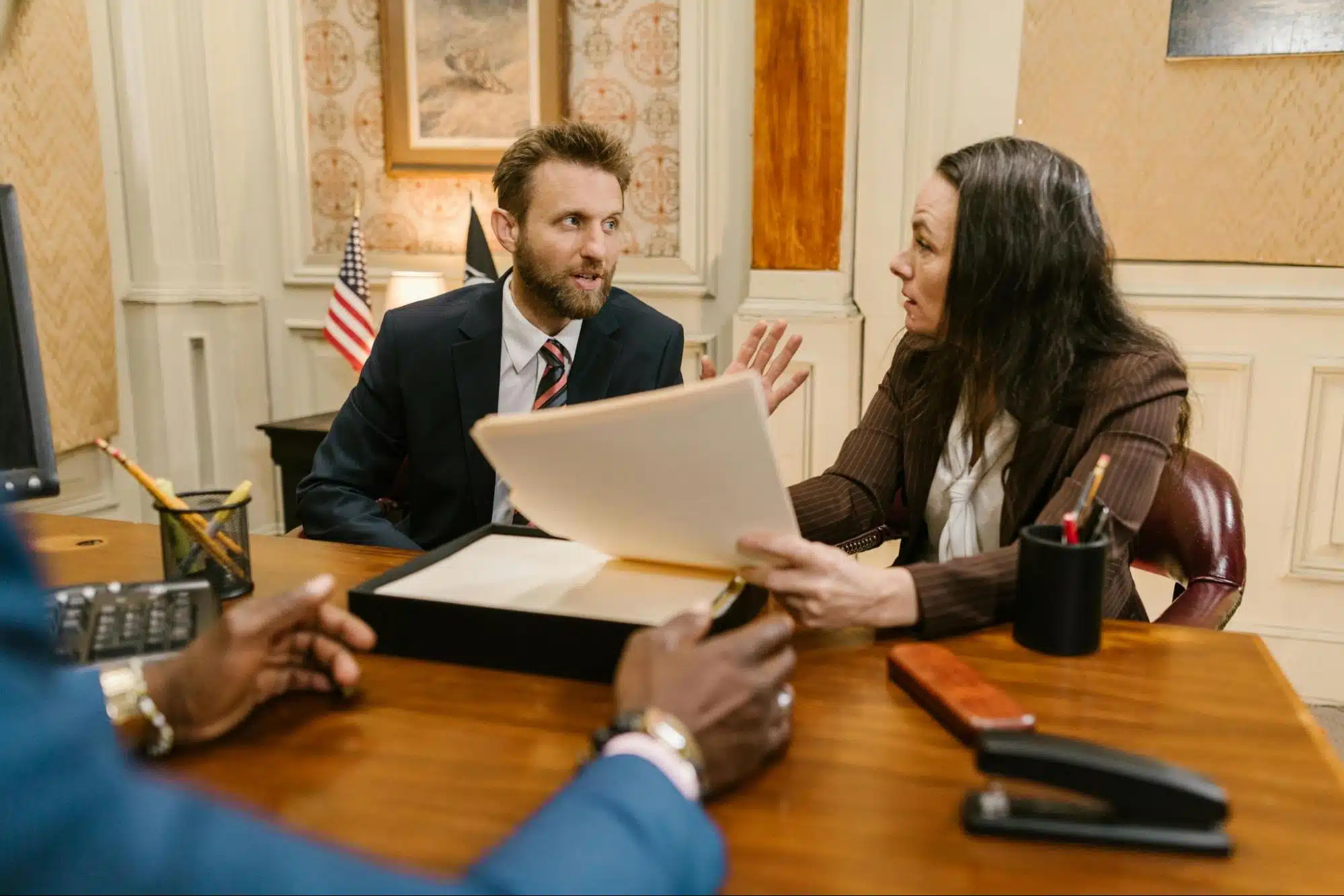 Three people in business attire having a discussion around a wooden desk