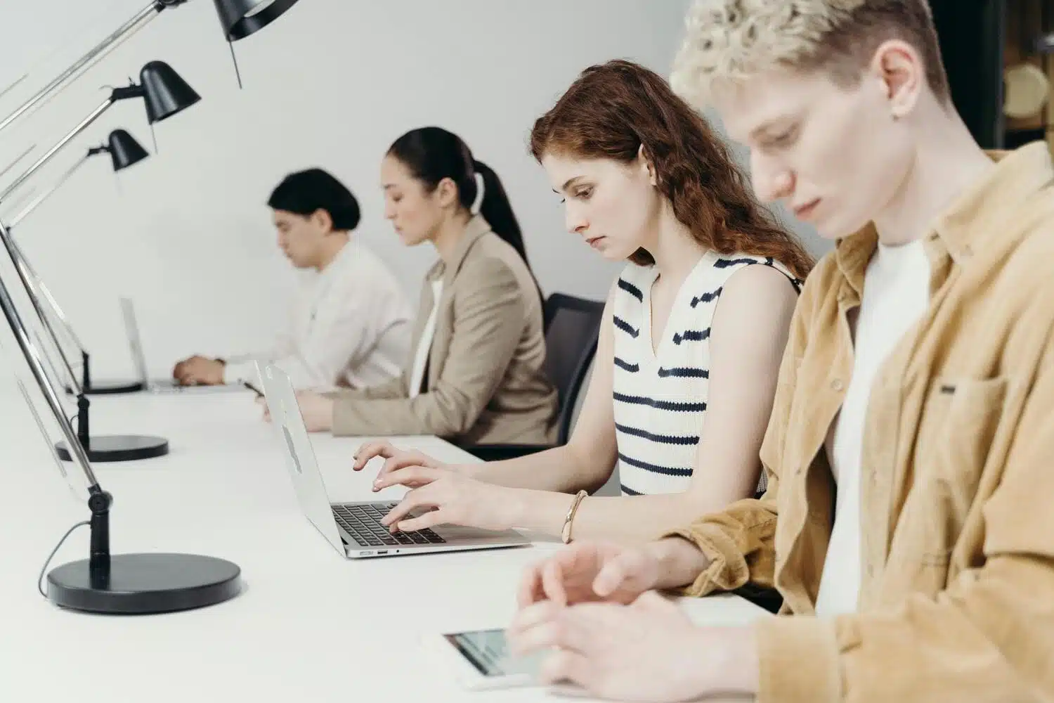 A row of professionals working on laptops and tablets at a long white desk